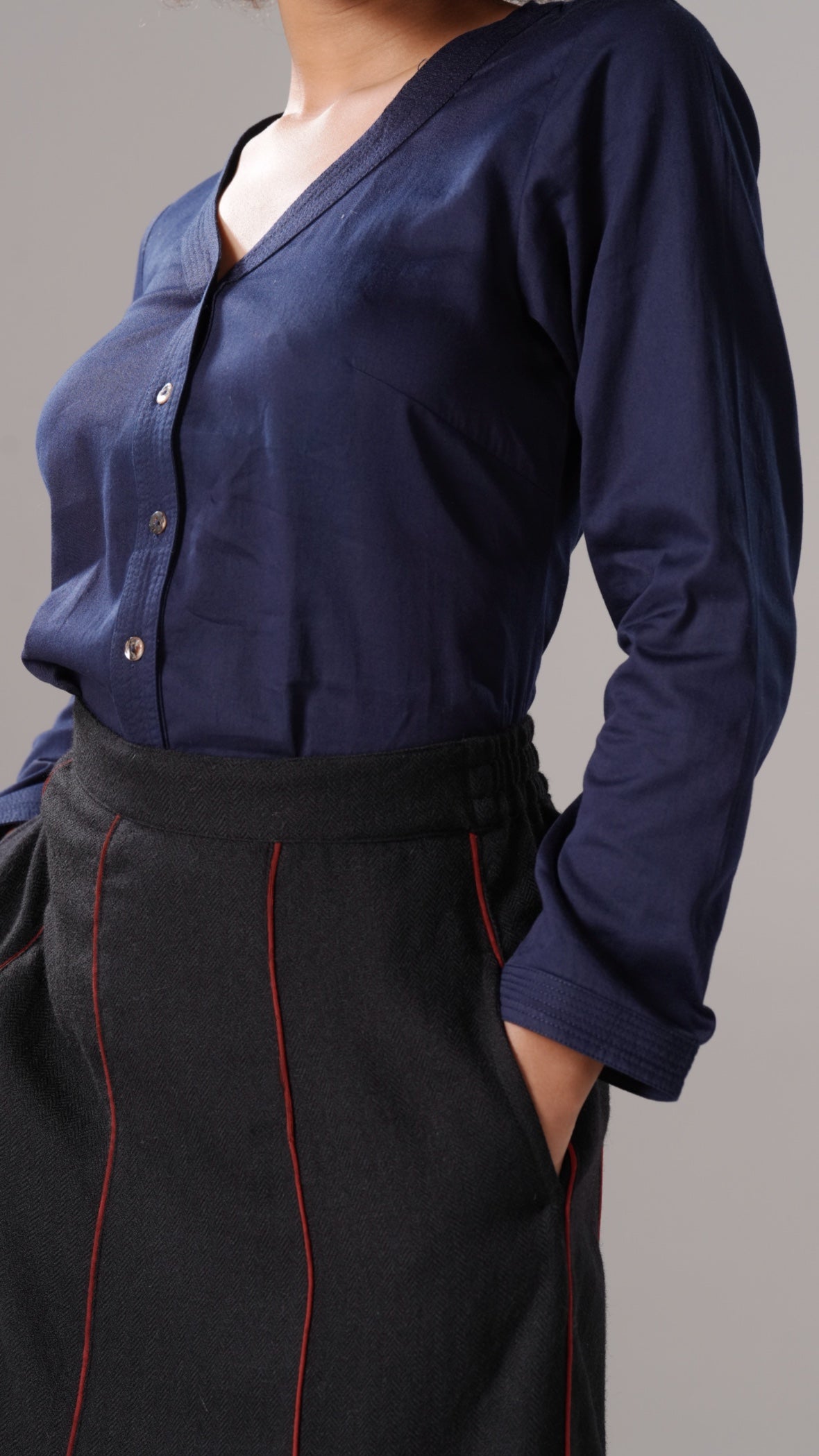 Person wearing a navy blue long-sleeve shirt and black pants with red piping on a gray background