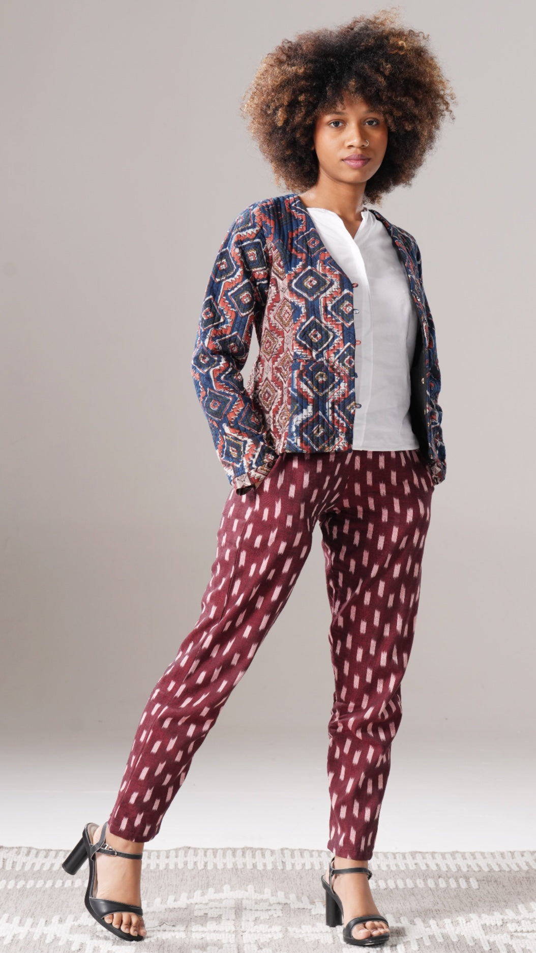Woman wearing a patterned jacket and maroon pants on a plain background