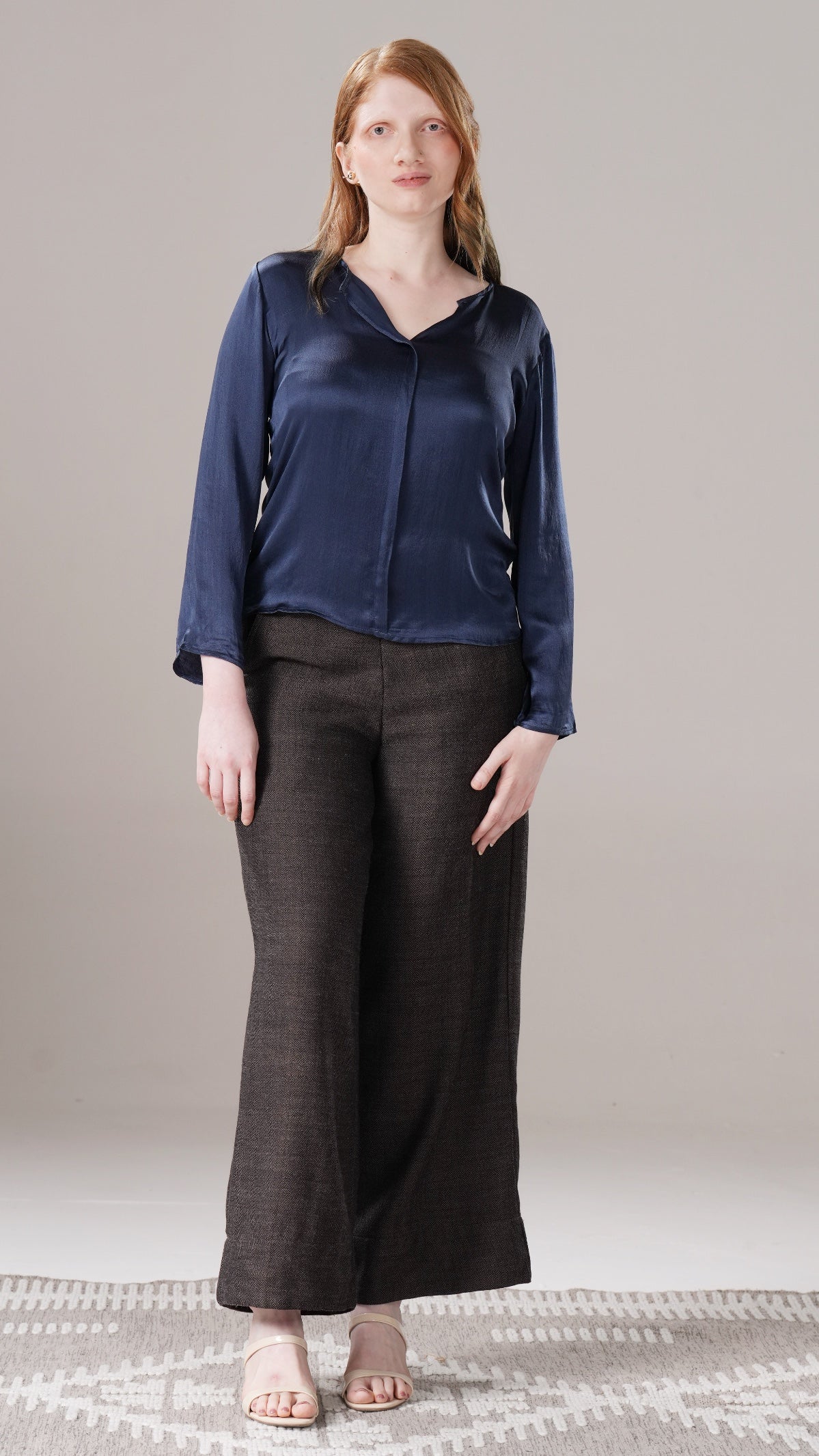 Woman wearing a blue top and black pants on a neutral background