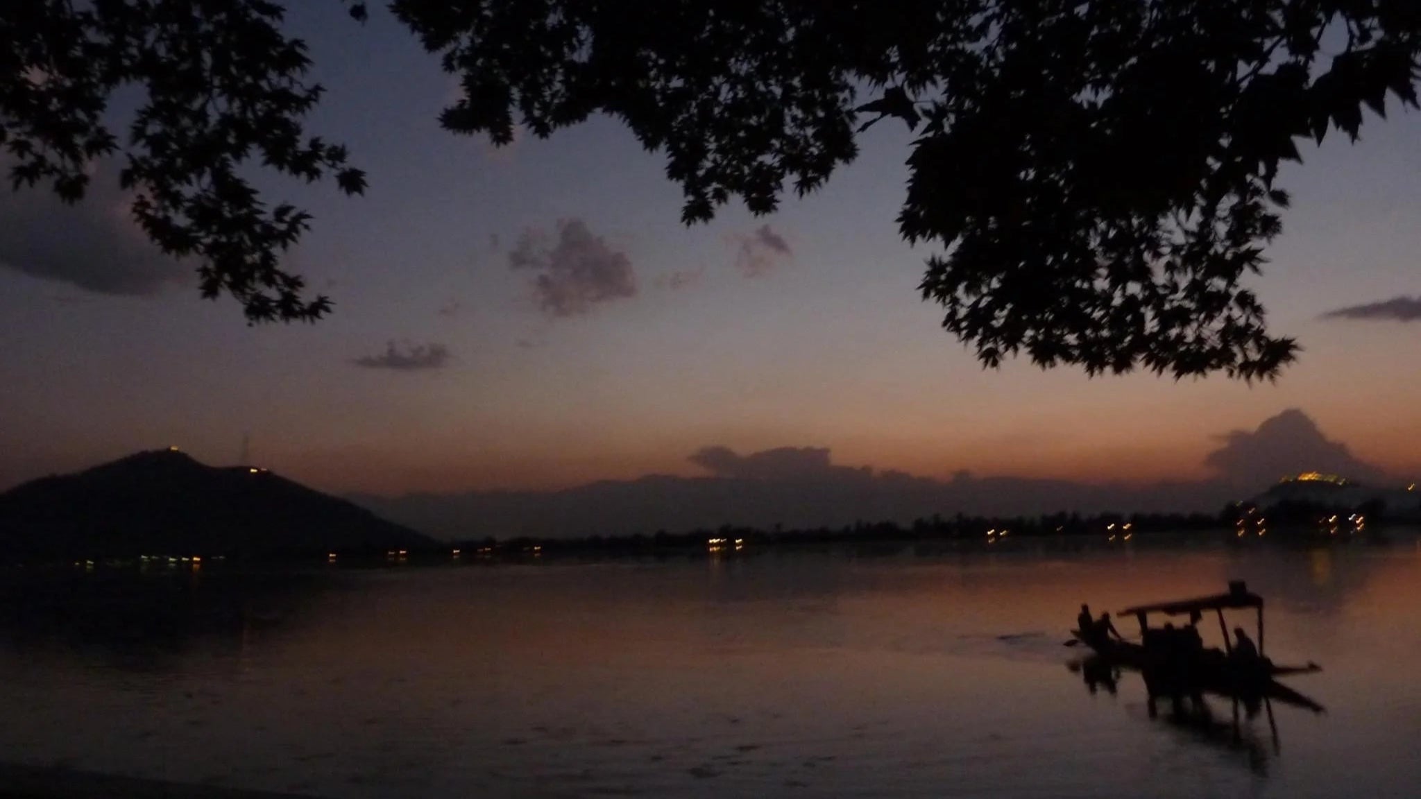 Dusk over a lake with silhouette of trees and distant lights.