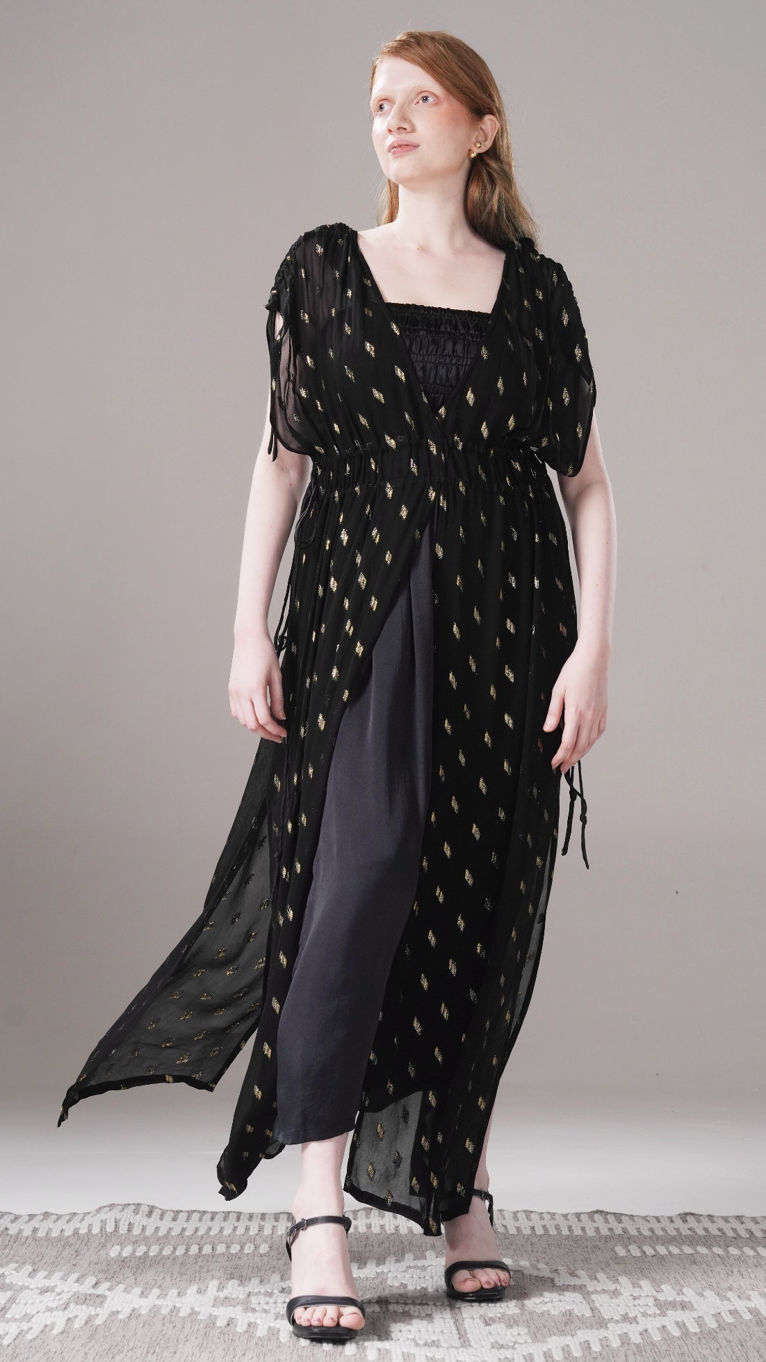 Woman wearing a black dress with gold patterns on a gray background