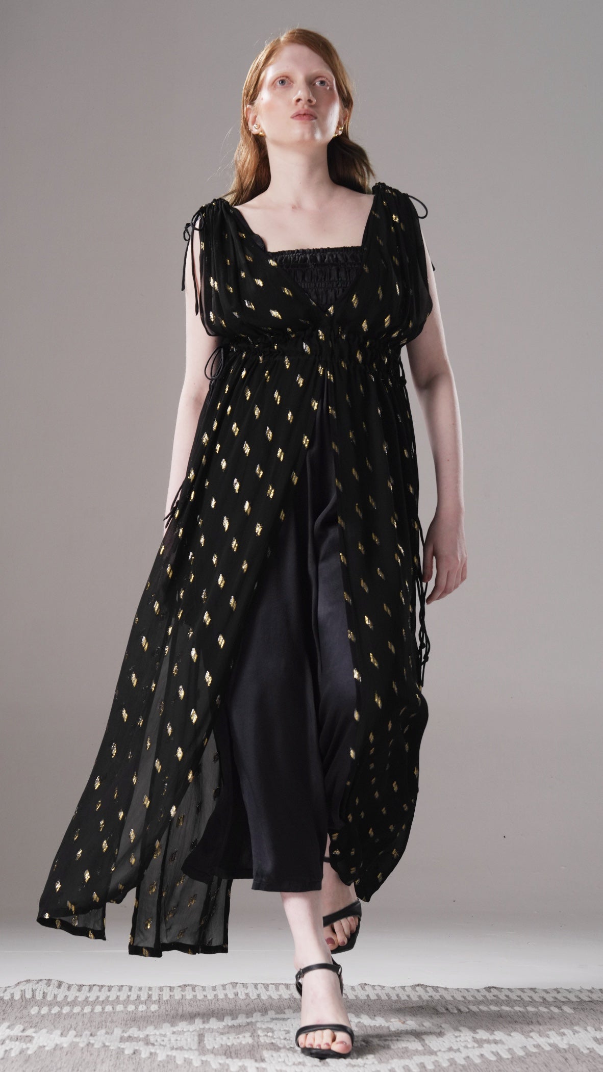 Woman wearing a black dress with gold patterns on a gray background