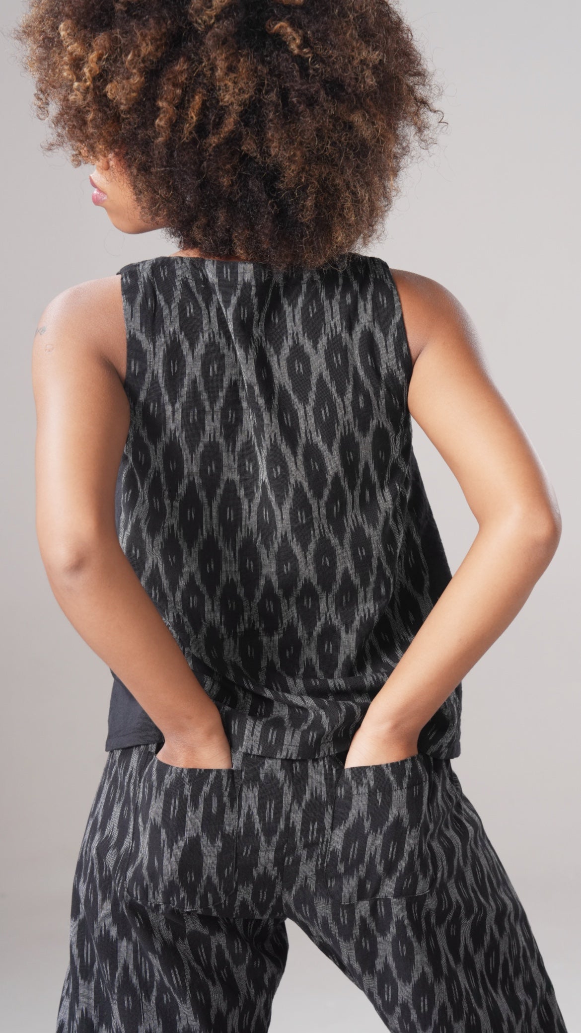 Person wearing a sleeveless top and pants with a black and gray pattern on a plain background