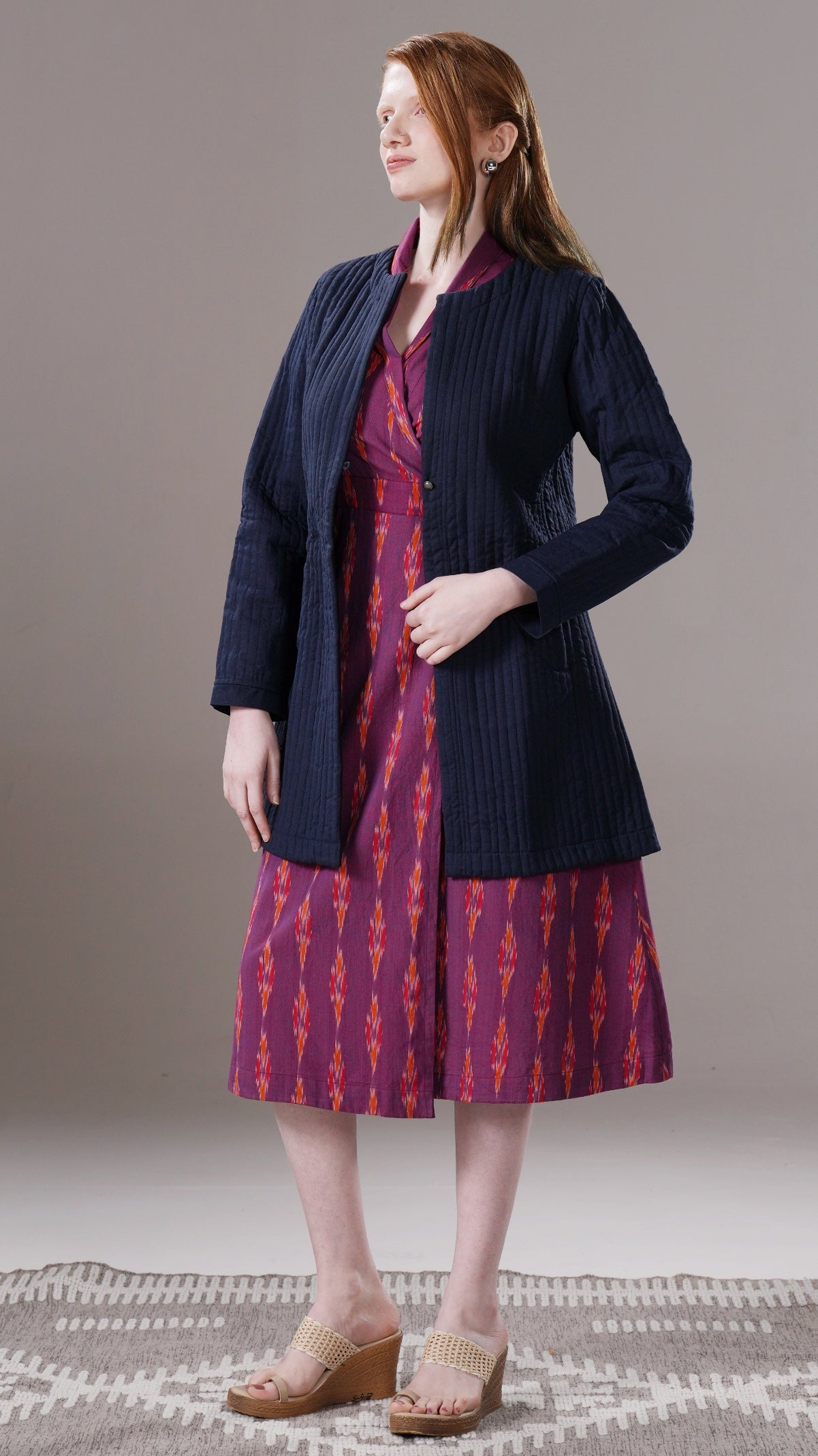 Woman wearing a dark blue cardigan over a patterned dress on a plain background