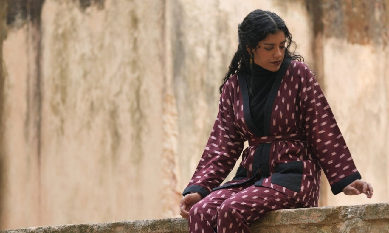 Woman in a patterned outfit sitting on a stone ledge with a blurred background