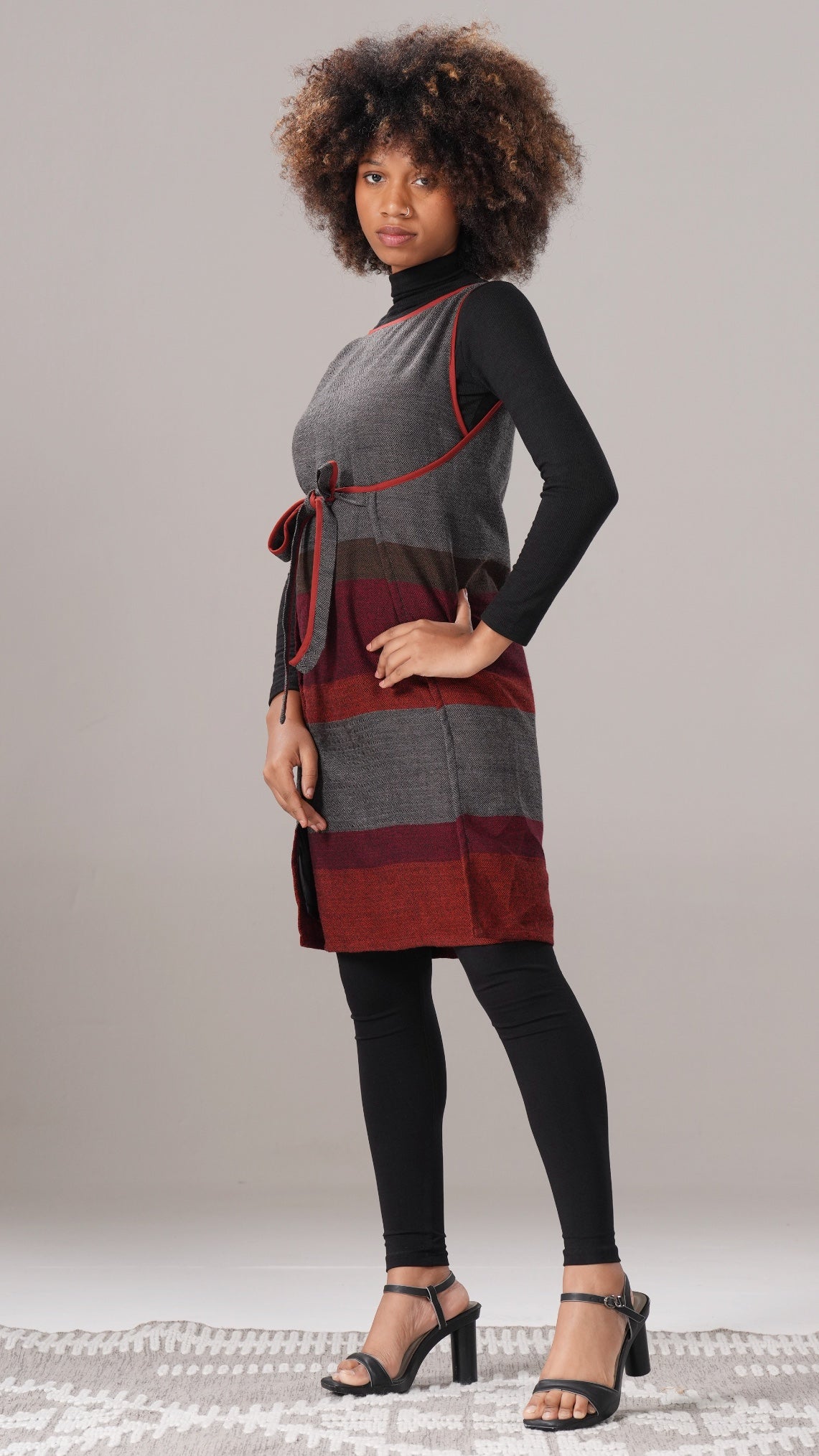Woman wearing a gray and red striped dress with black tights and shoes on a neutral background
