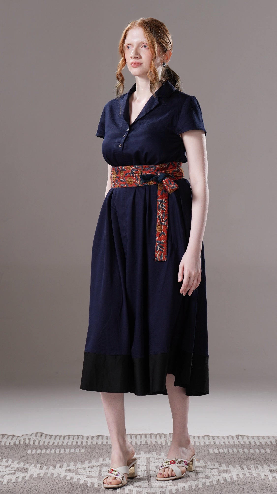 Woman wearing a navy dress with a patterned belt on a neutral background