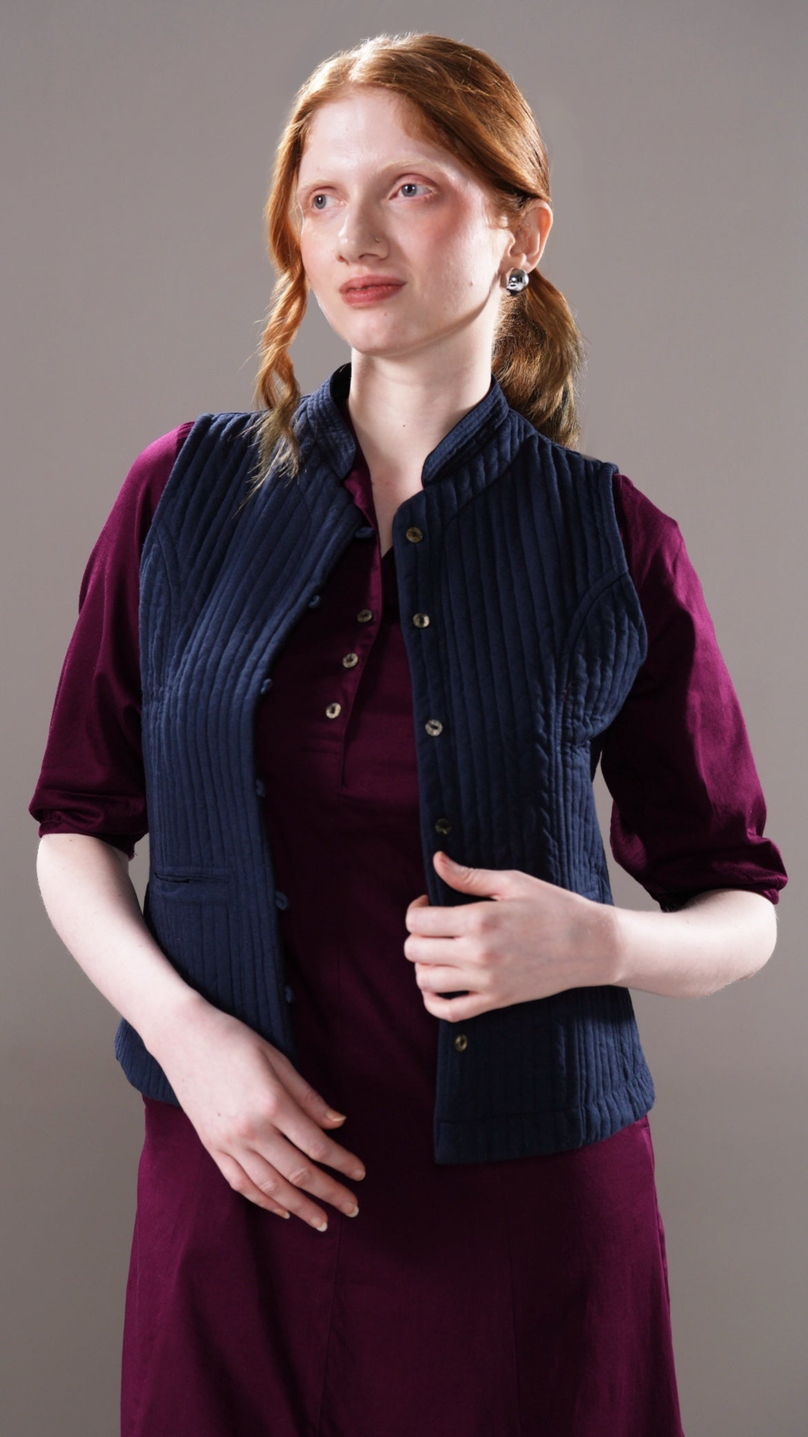Woman wearing a navy vest over a purple shirt against a gray background