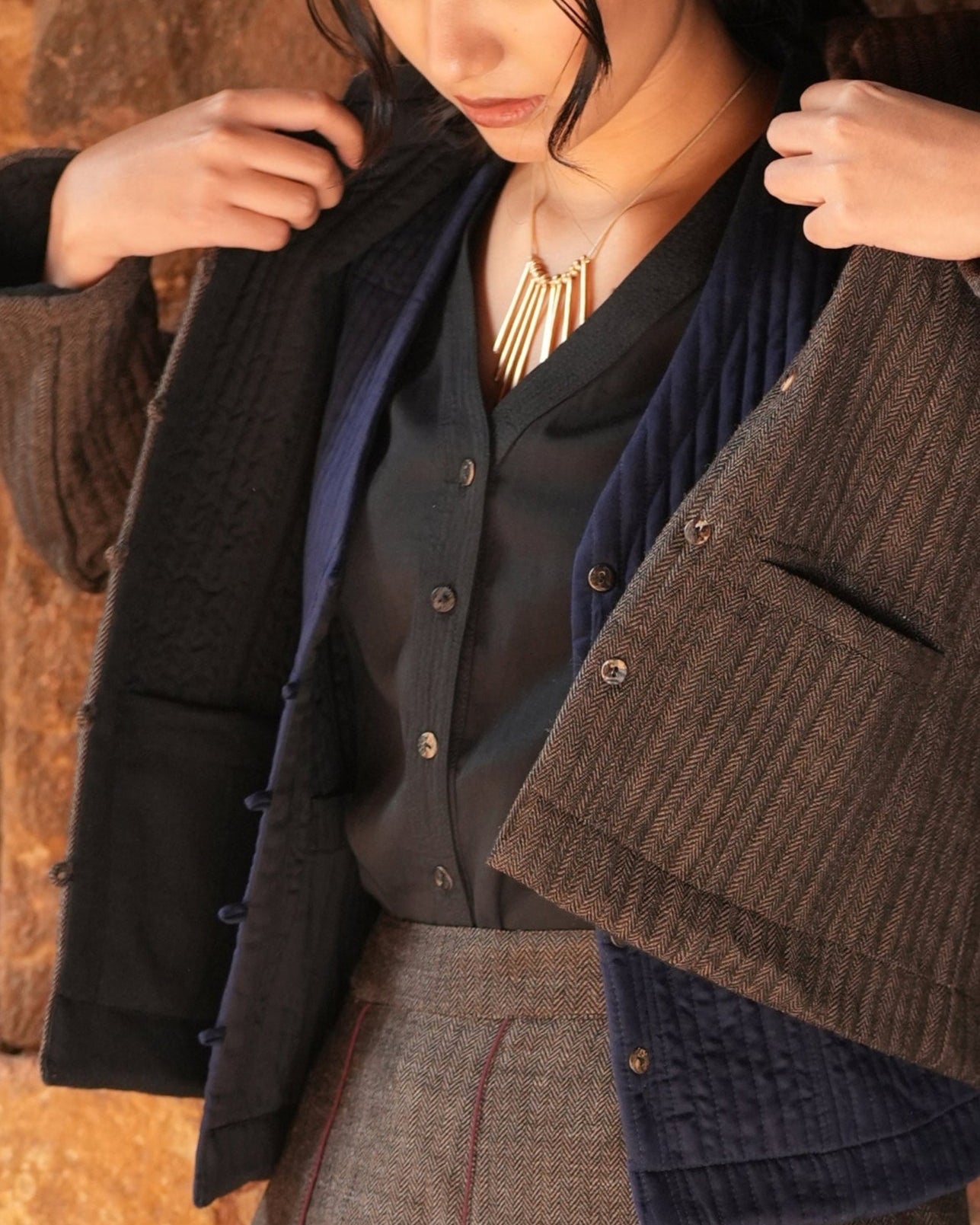 Person wearing a layered outfit with a dark shirt, brown jacket, and blue vest.