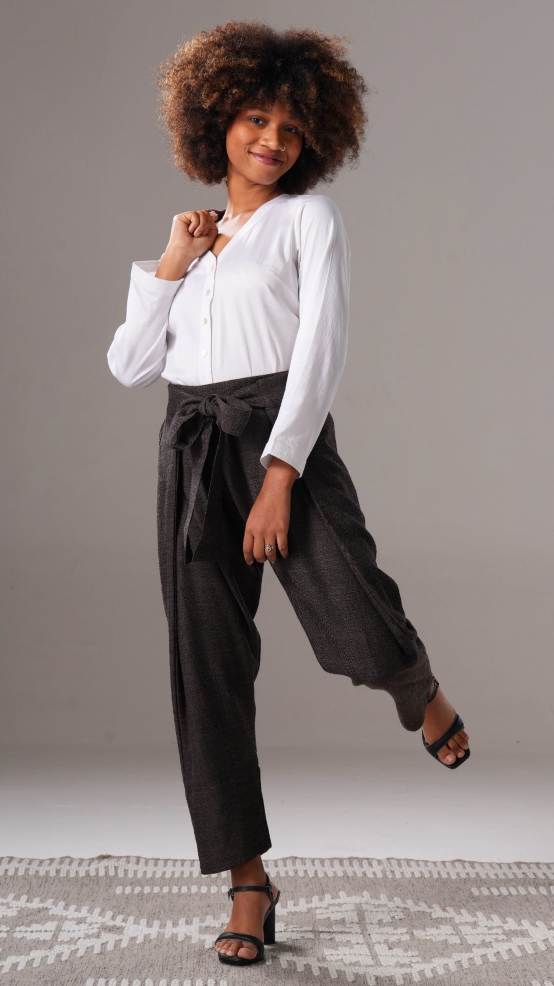 Woman wearing a white blouse and dark pants on a plain background