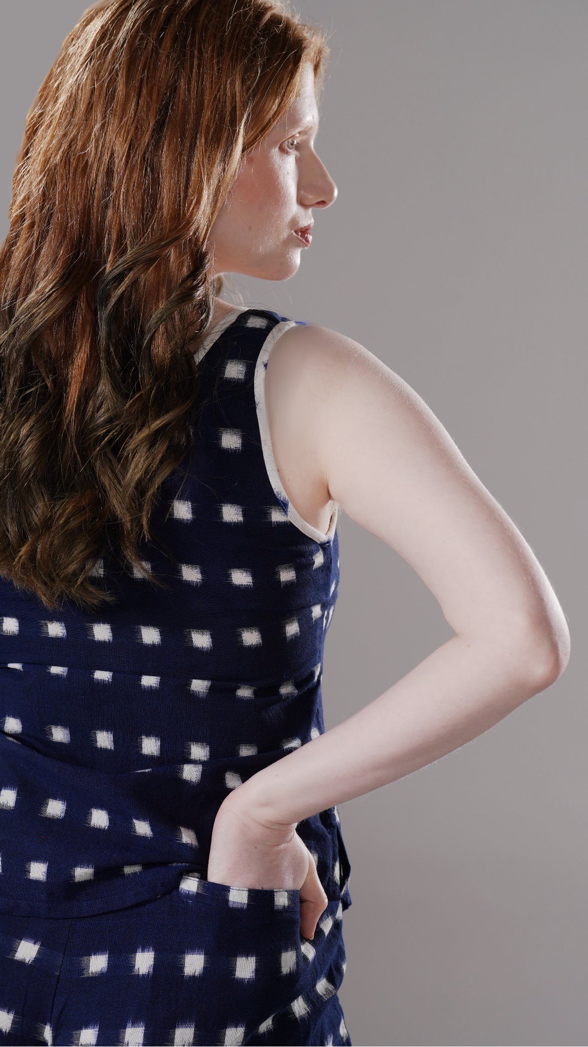 Woman wearing a navy blue dress with white polka dots against a gray background