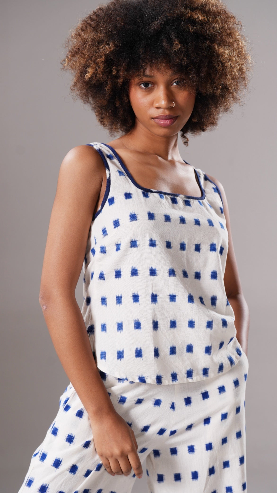 Woman wearing a white sleeveless top with blue square pattern and matching pants against a gray background
