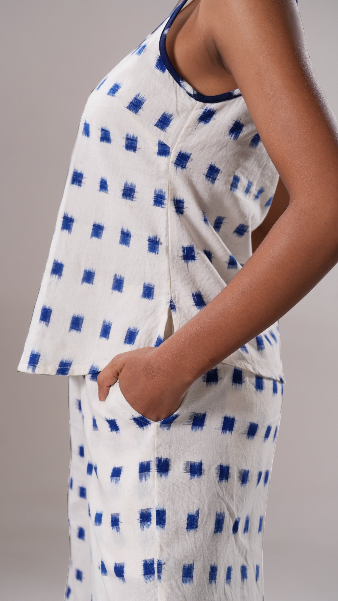 White sleeveless top with blue square pattern worn by a person on a gray background