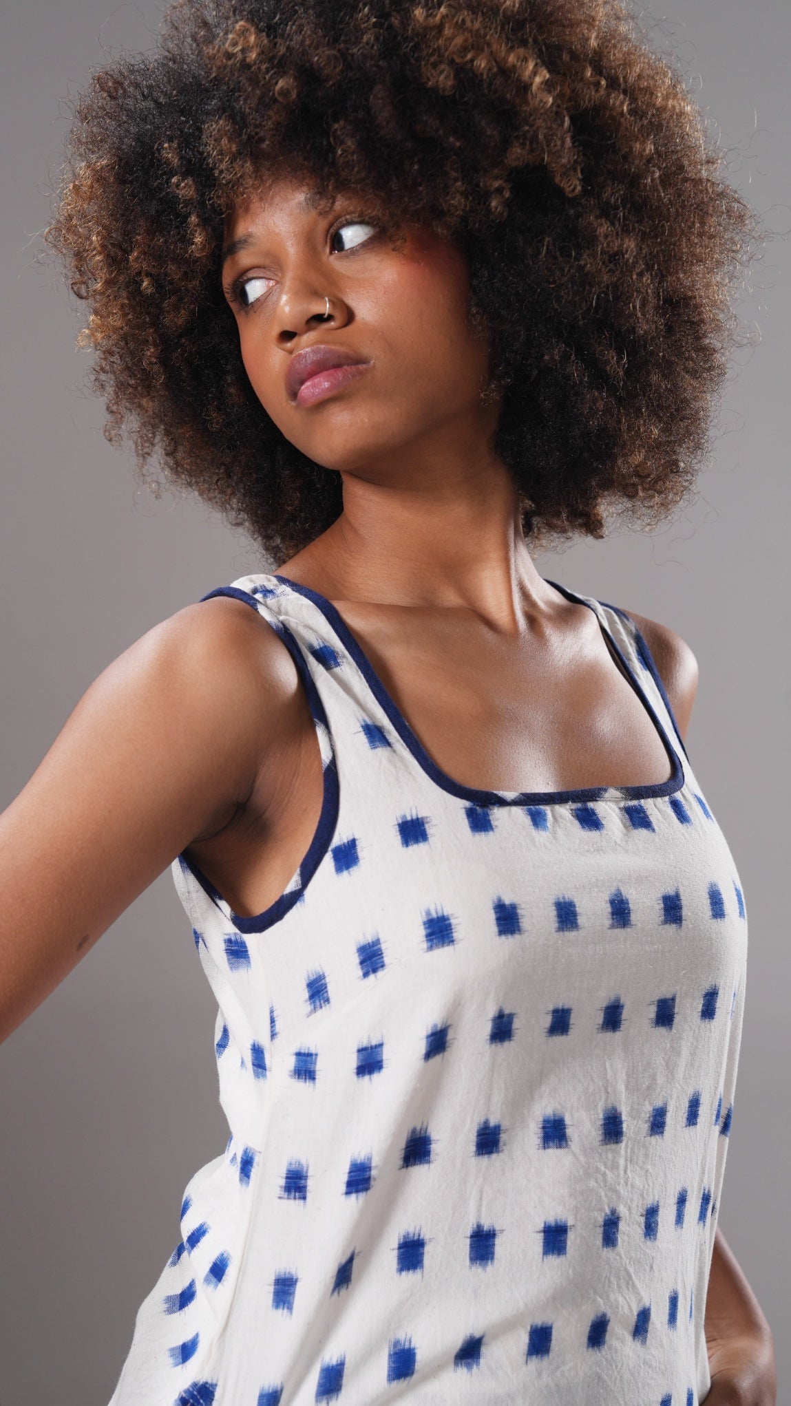 Woman wearing a white sleeveless top with blue patterns against a gray background