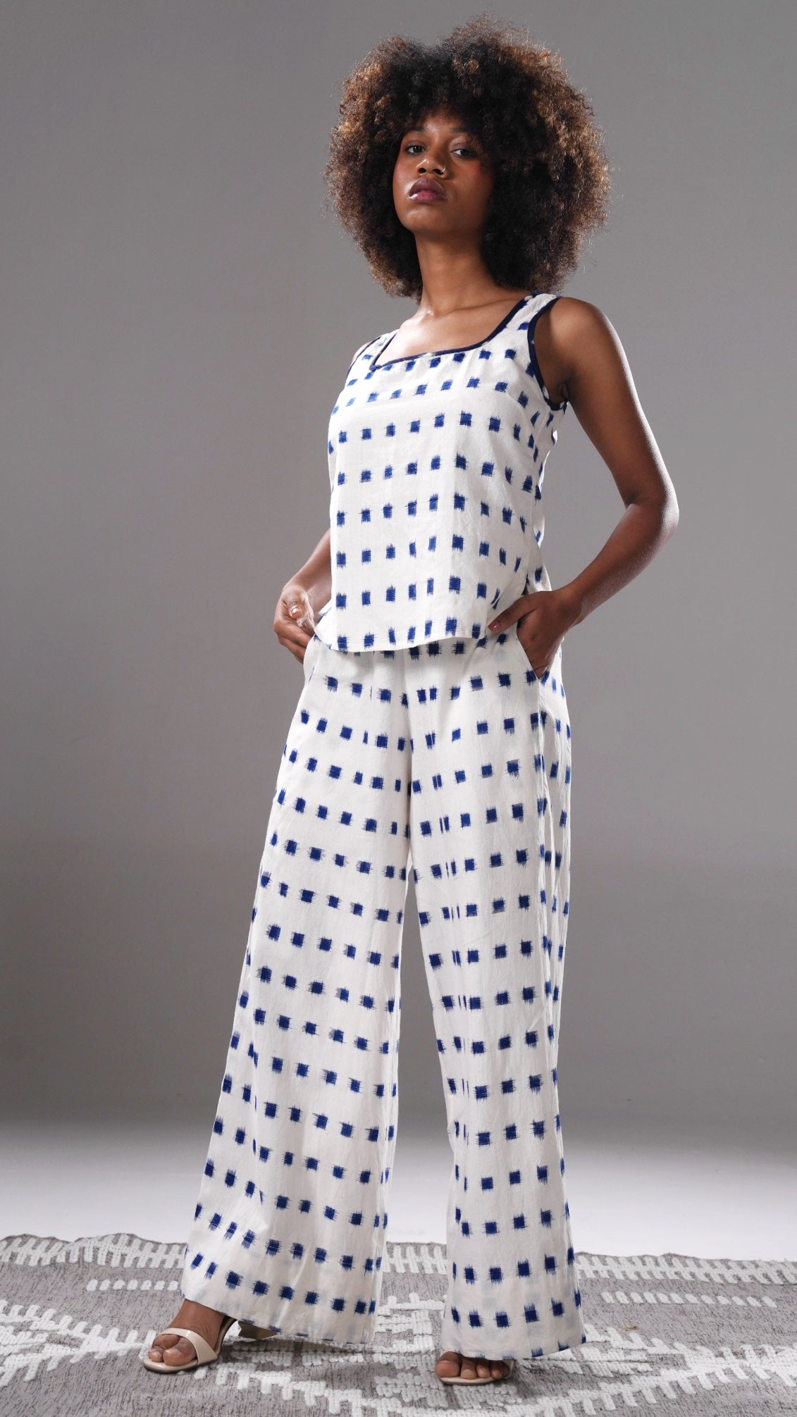 Woman wearing a white top and blue checkered pants against a gray background