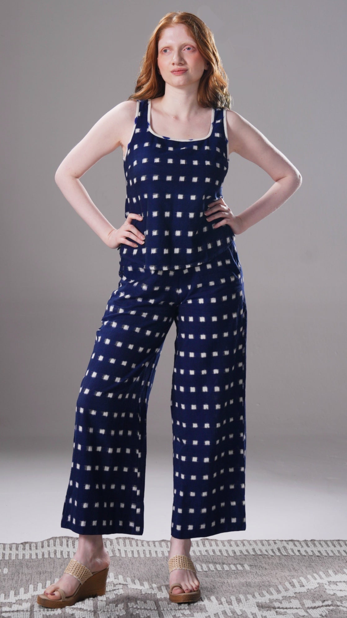 Woman wearing a navy blue polka dot jumpsuit on a gray background