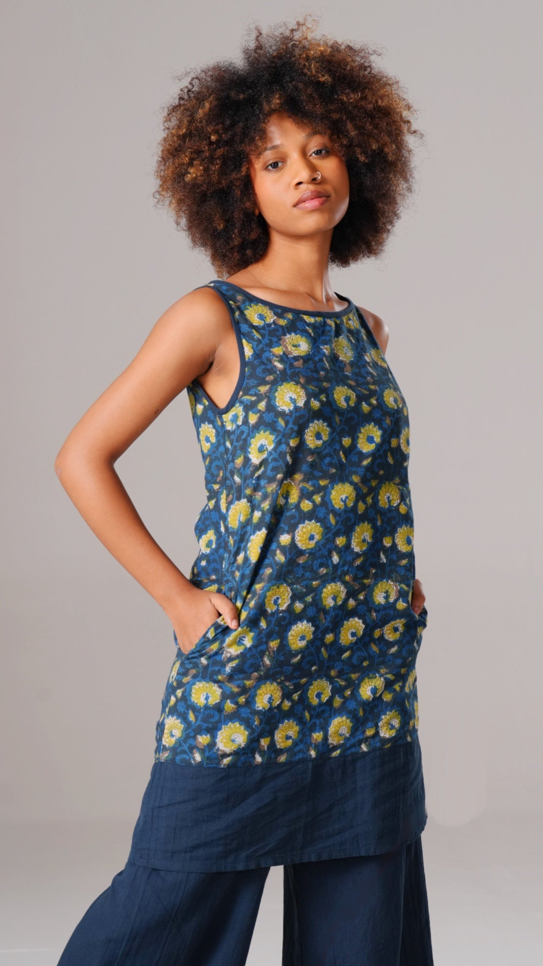 Woman wearing a blue floral sleeveless top and dark pants on a gray background