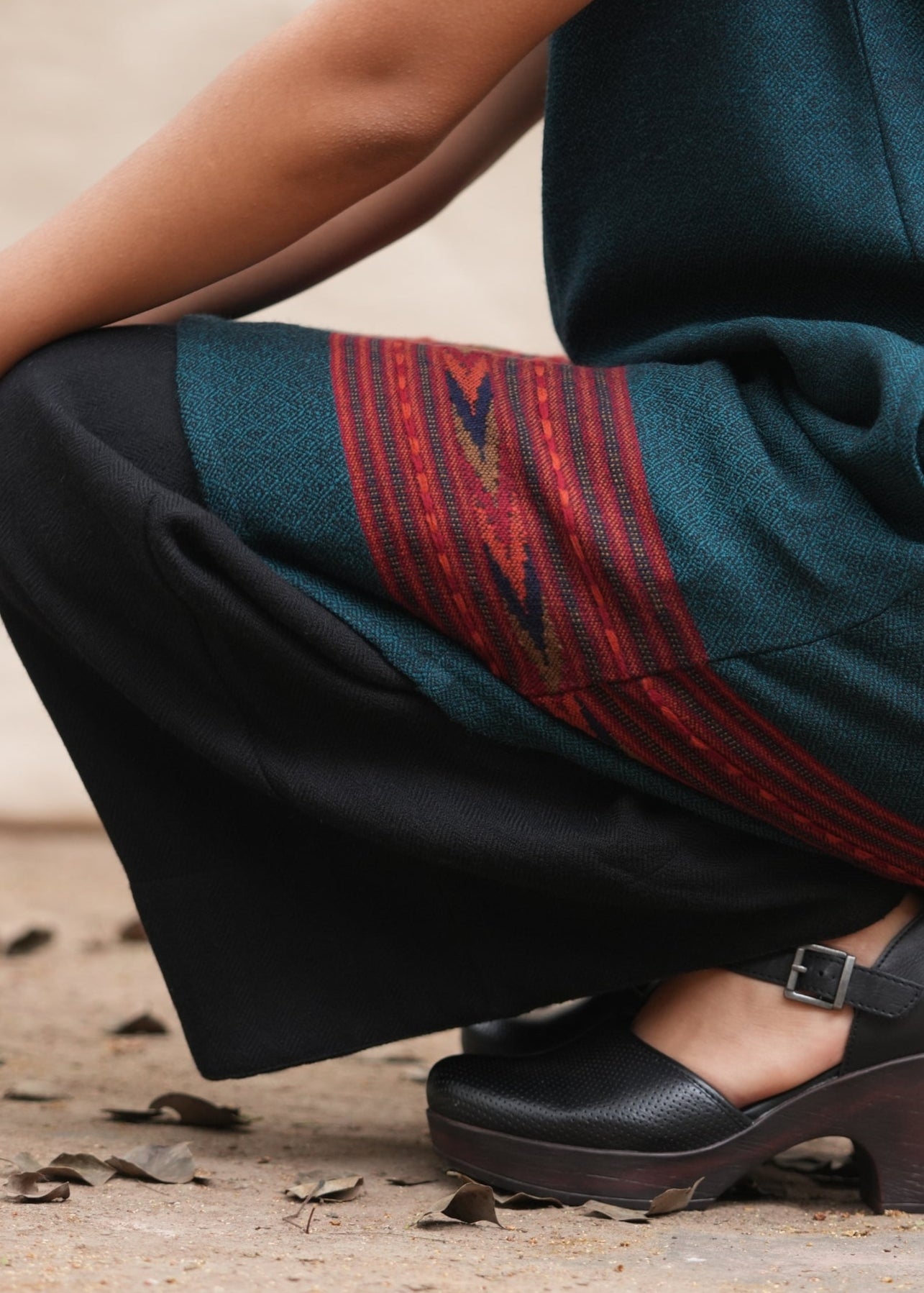 Person wearing a dark green skirt with red patterns and black shoes on a natural background