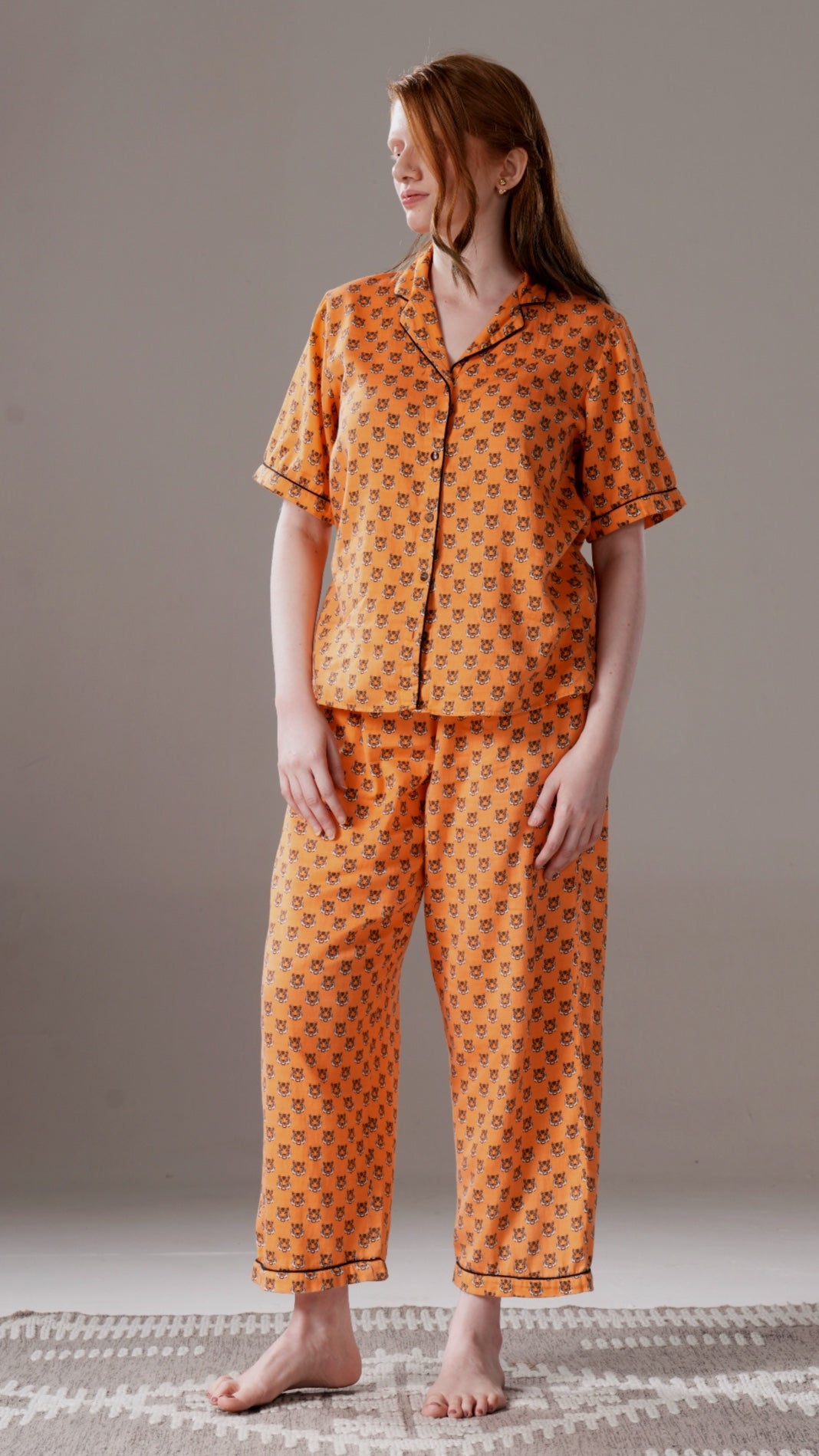 Woman wearing an orange patterned pajama set on a neutral background