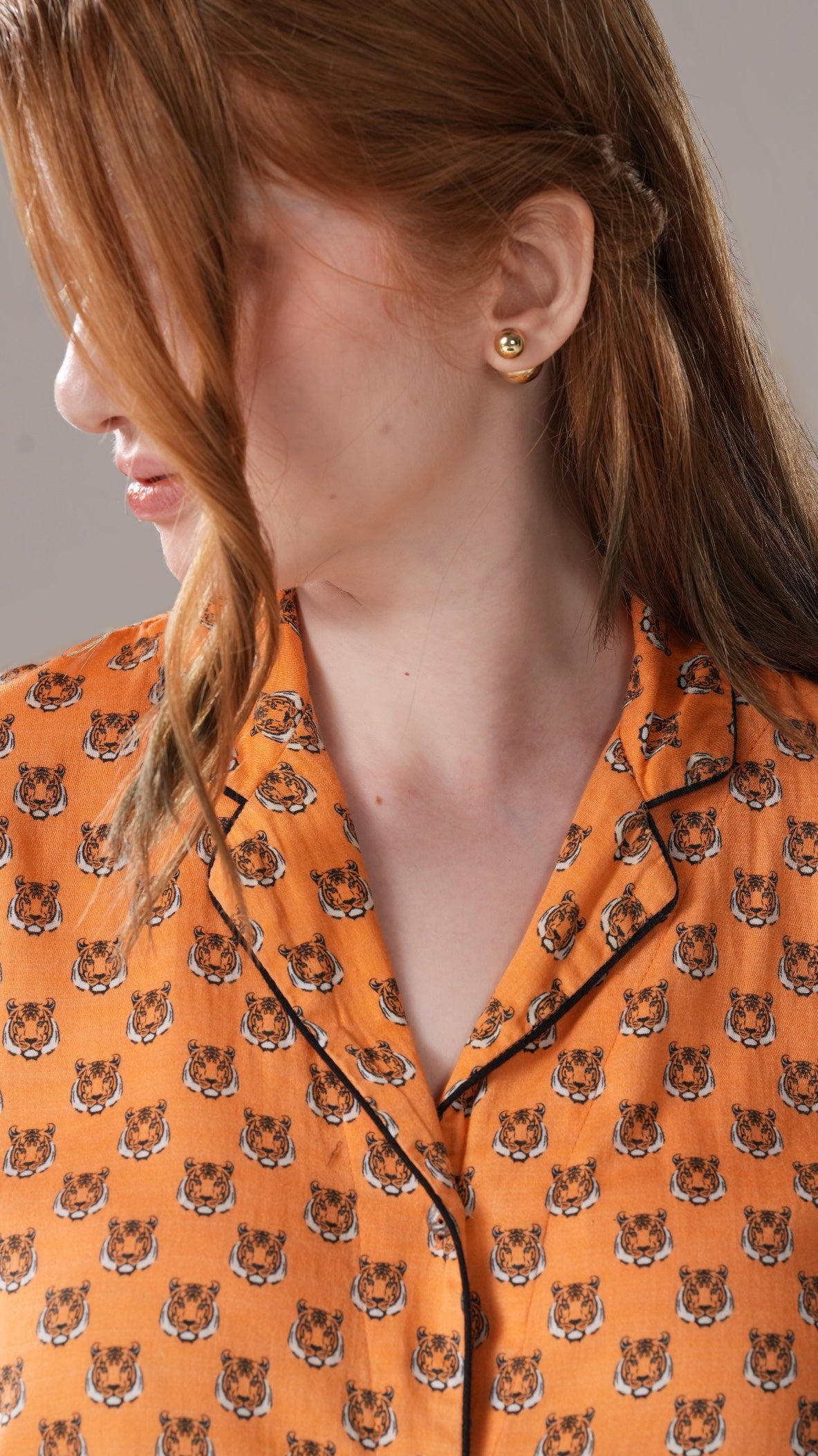 Person wearing an orange shirt with tiger pattern and gold earrings.